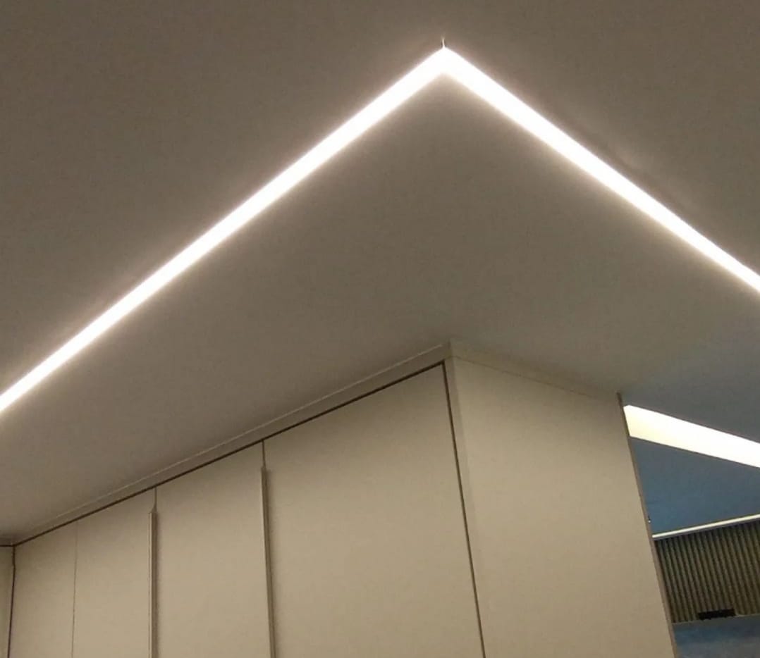 teto branco com faixas de LED formando um pico em V invertido sobre armários embutidos brancos